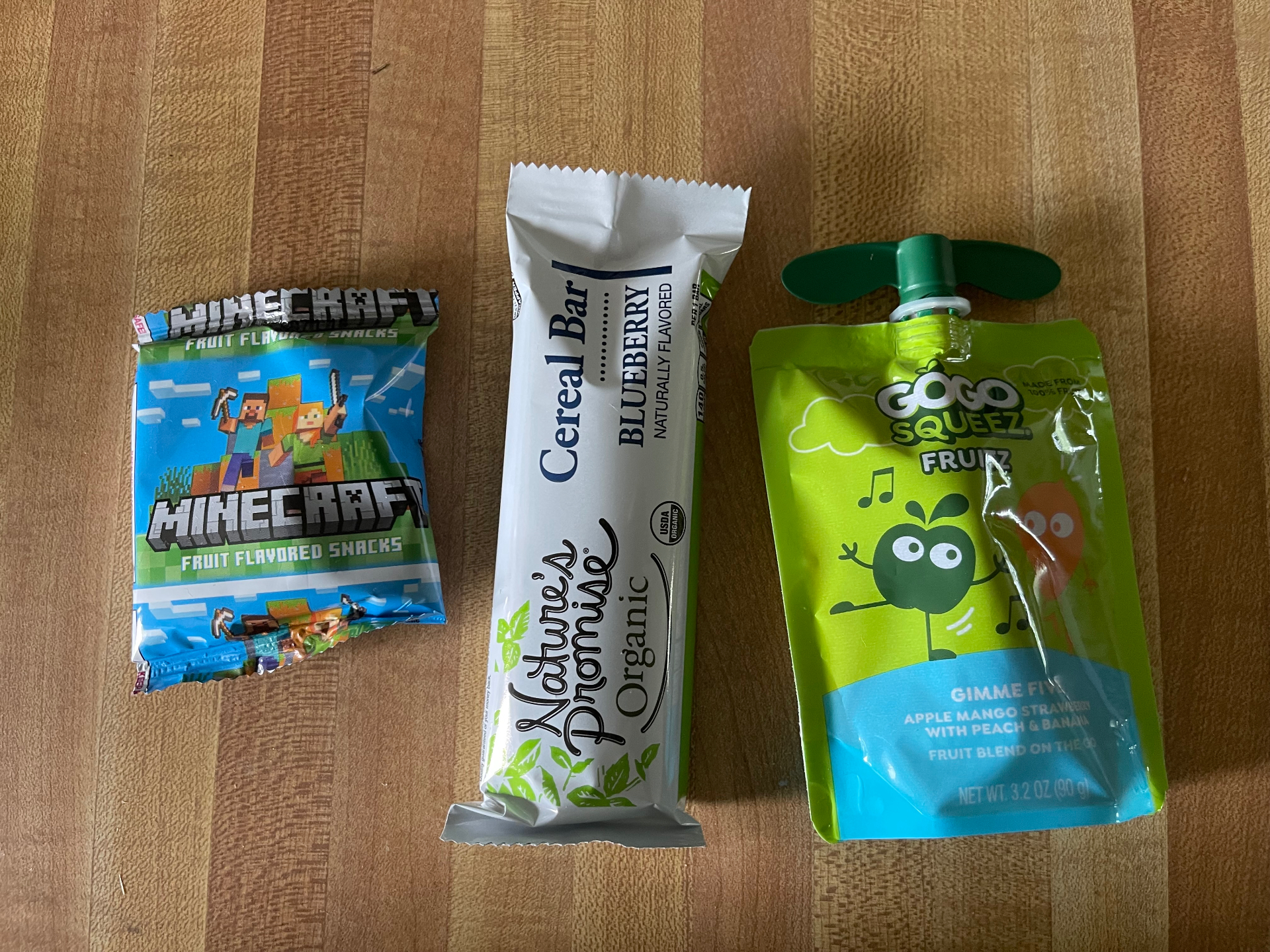 Minecraft fruit snacks, a blueberry cereal bar, and a GoGo Squeez pouch on a wooden table