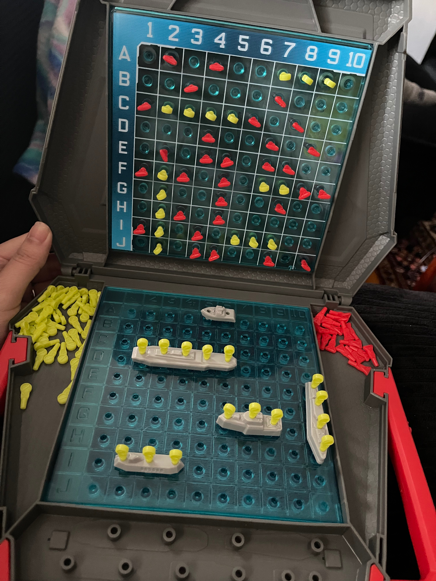 An open Battleship game with red and yellow pegs scattered across the board