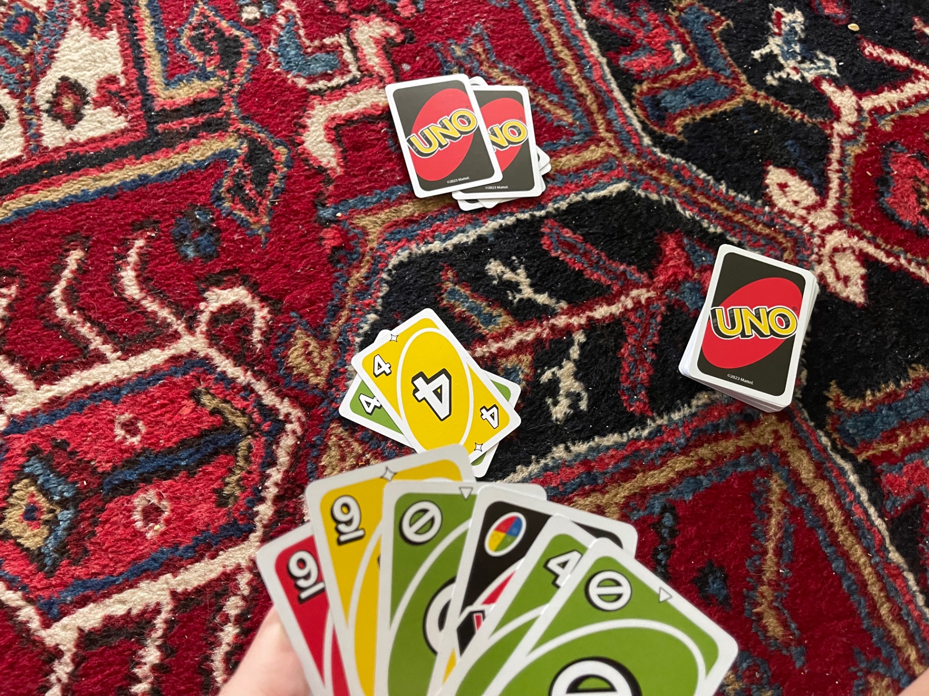 A hand of UNO cards held above a red Persian rug with a draw pile and discard pile